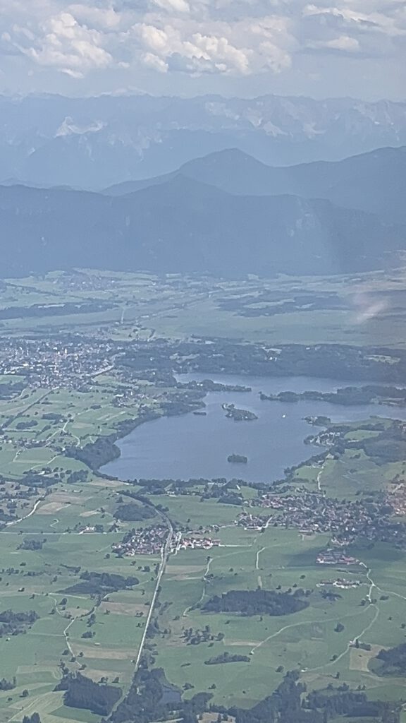 Blick aus dem Flugzeug auf dem Weg zur Zugspitze: das Alpenvorland am Peißenberg mit einem See, dahinter die Alpen