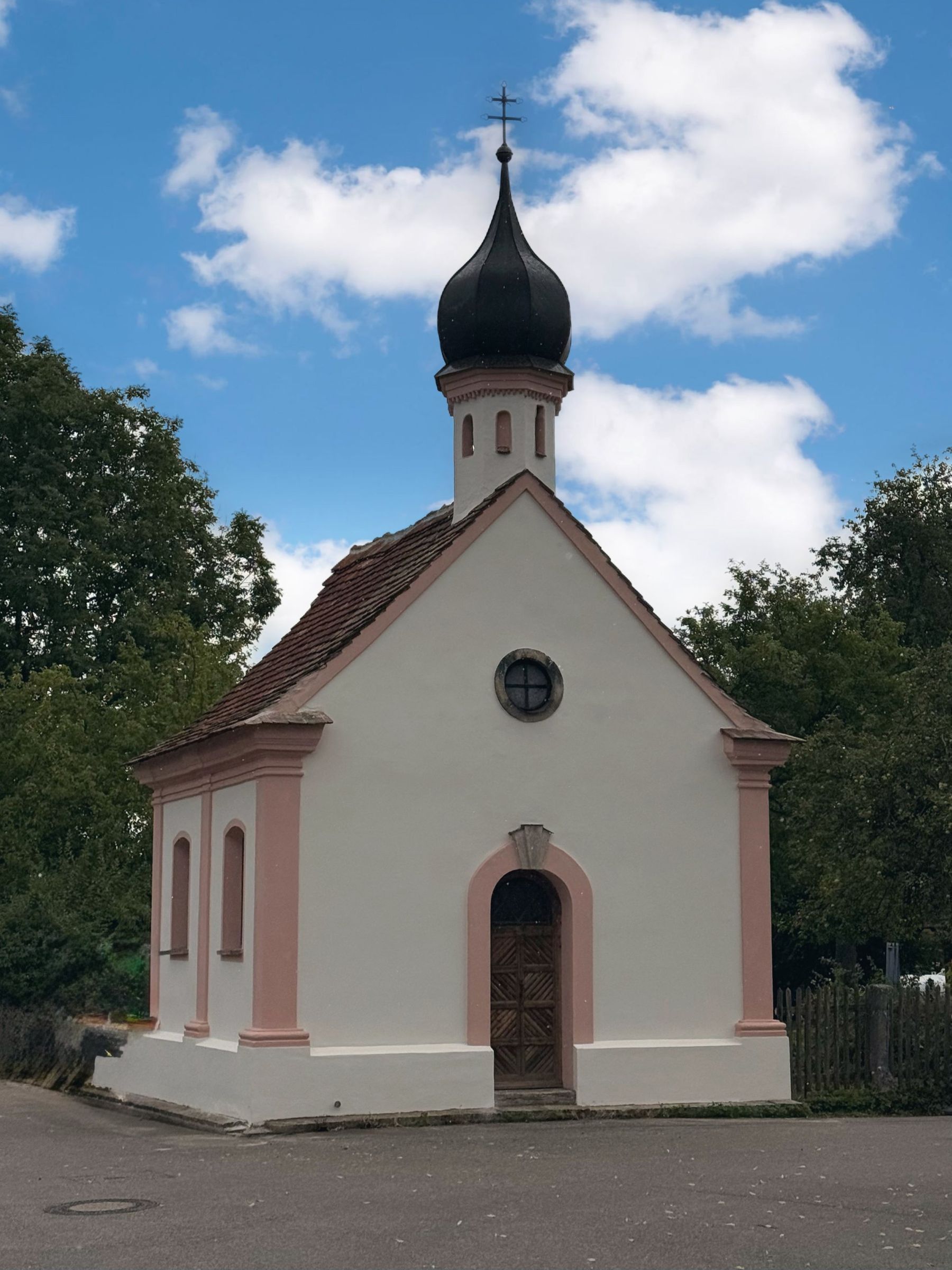 Hofkapelle Maria Hilf: weiß-rosa Barockkapelle mit Zwiebelturm vor blauem Himmel