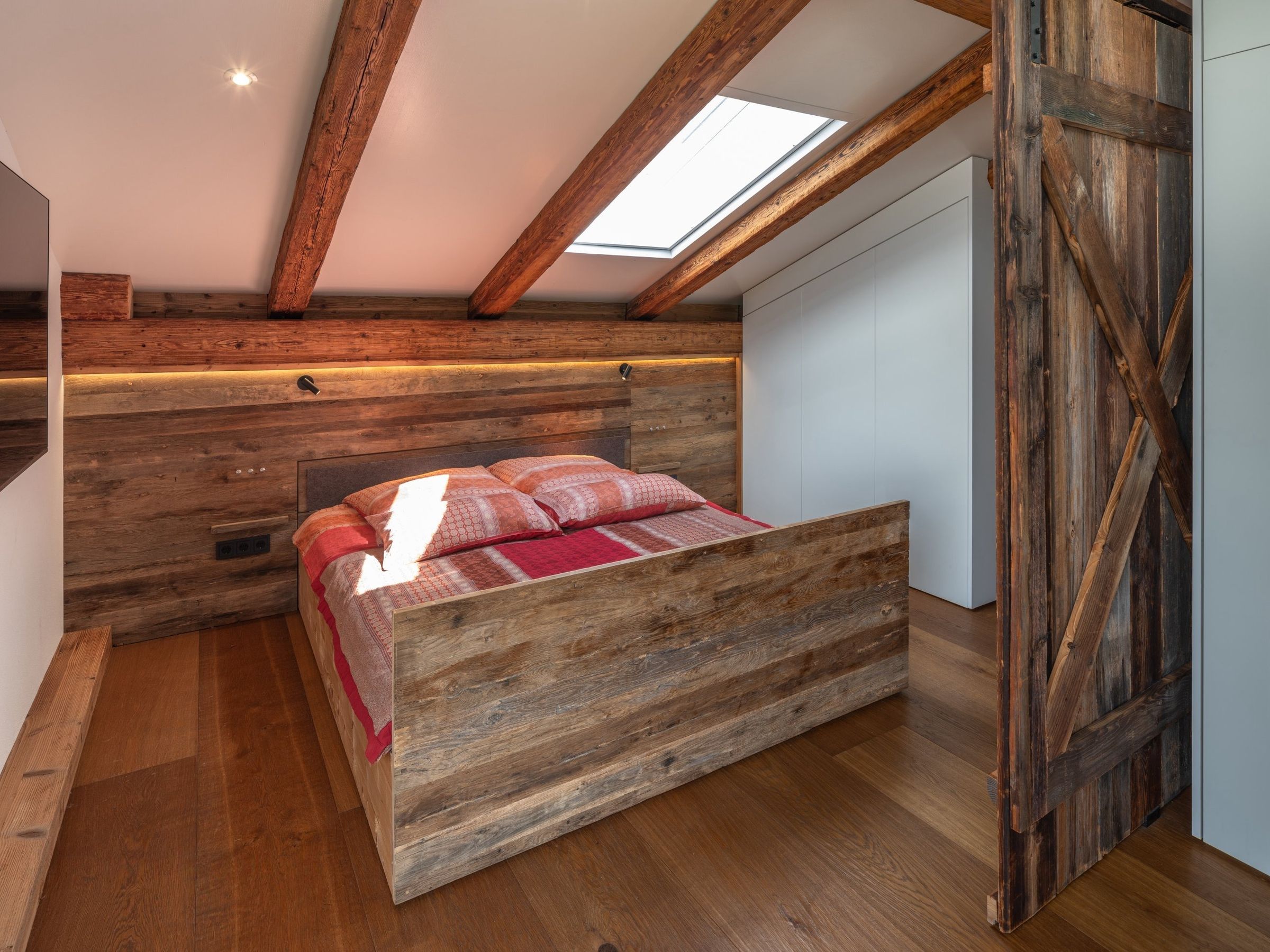Penthouse: reclaimed-wood double bed raised out of the knee wall beneath roof beams, next to the barn door